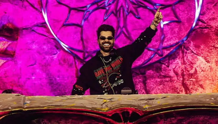 Alok de óculos escuros com a camisa Rave The World em cima do palco de um festival