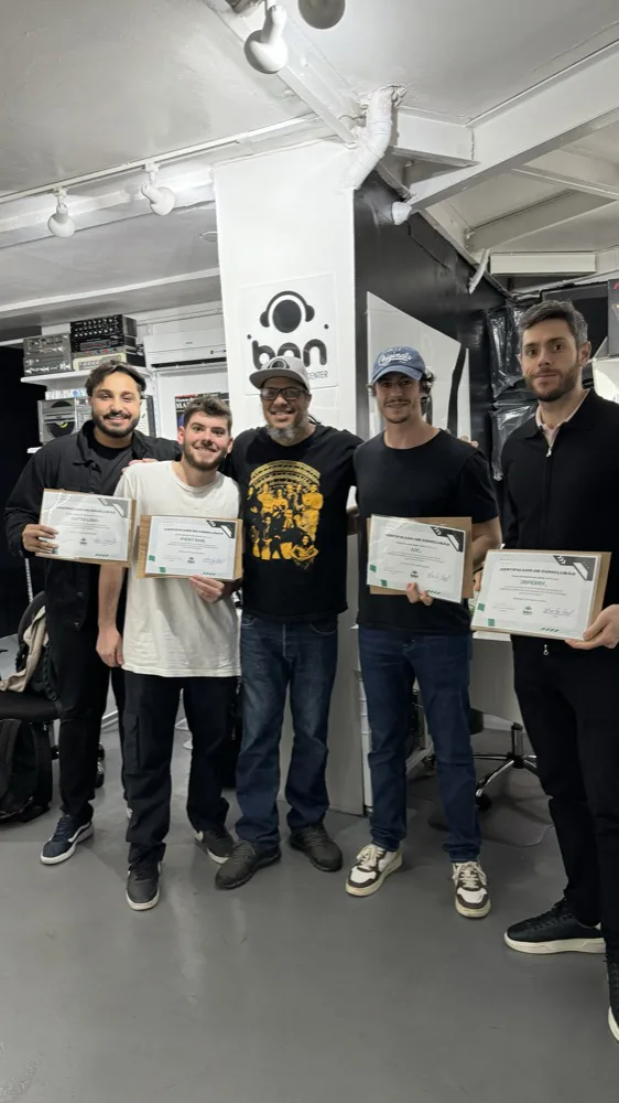 Cinco alunos da DJ Ban EMC sorrindo, segurando certificados de conclusão de curso no estúdio da escola