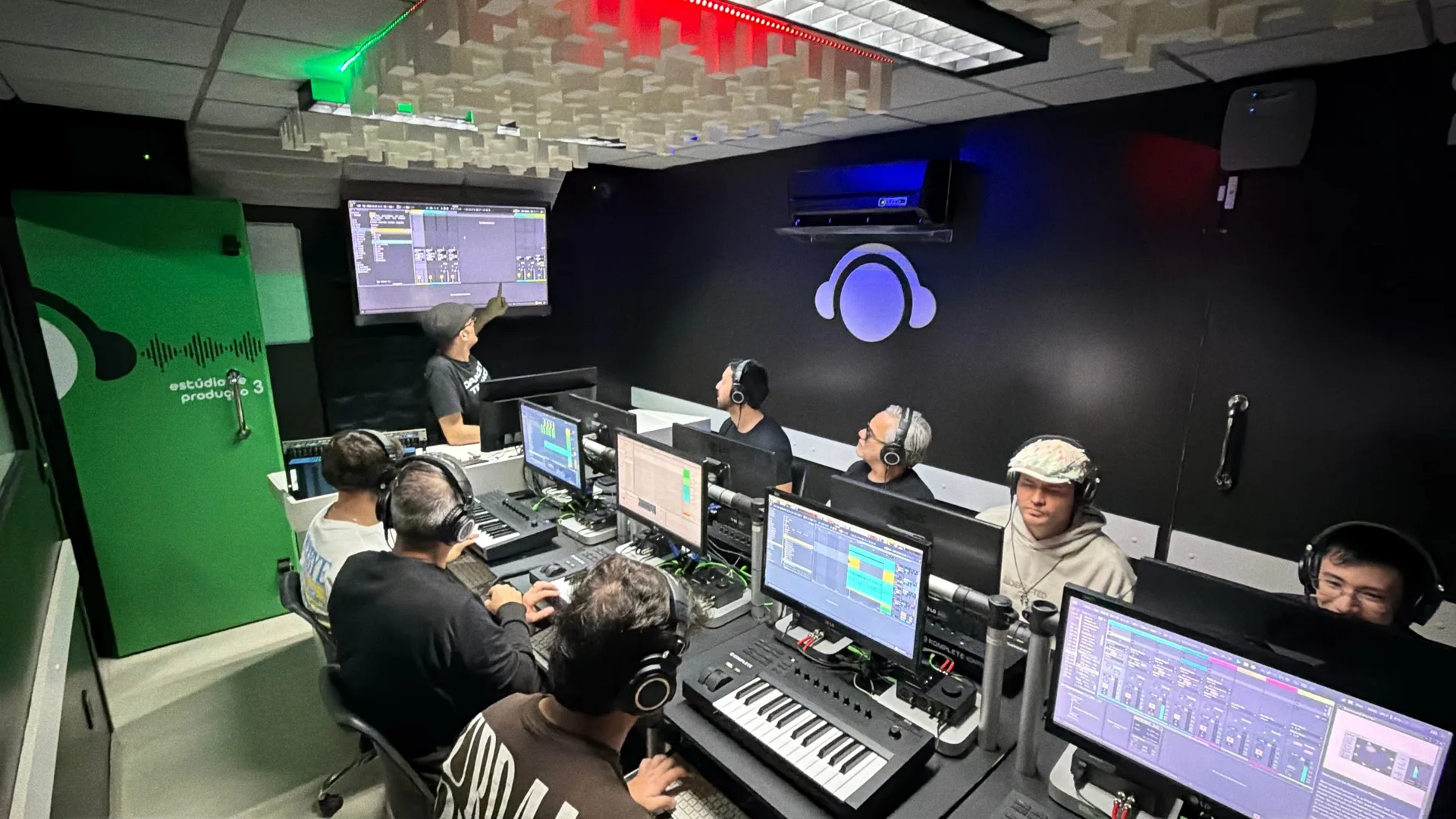 Turma de produção musical trabalhando em estações com teclado e monitores no estúdio 3 da DJ Ban EMC
