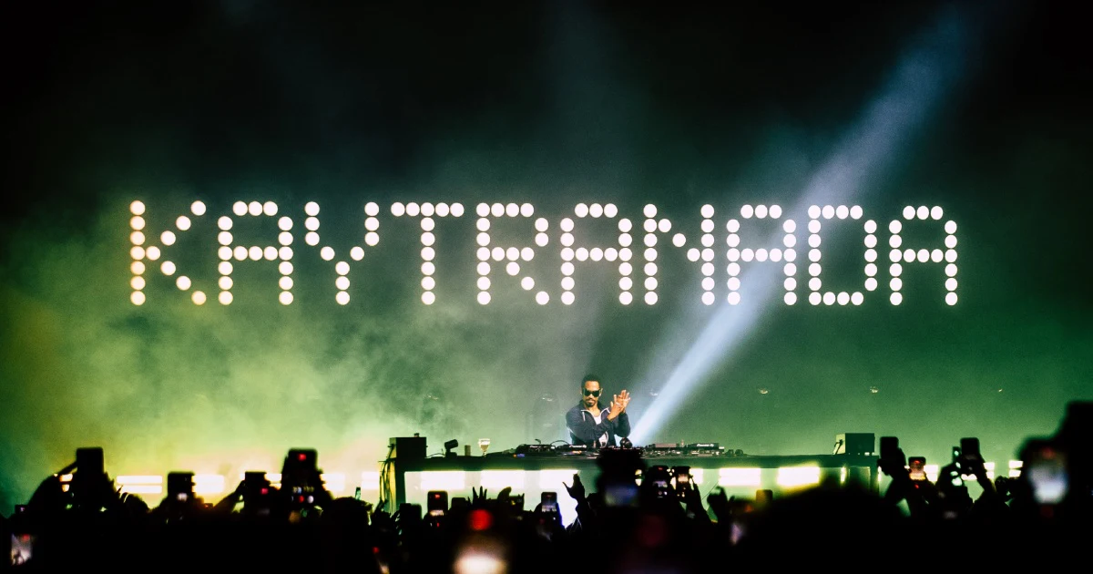 KAYTRANADA tocando no palco com o nome dele em letreiro de lâmpadas e o público de celular erguido