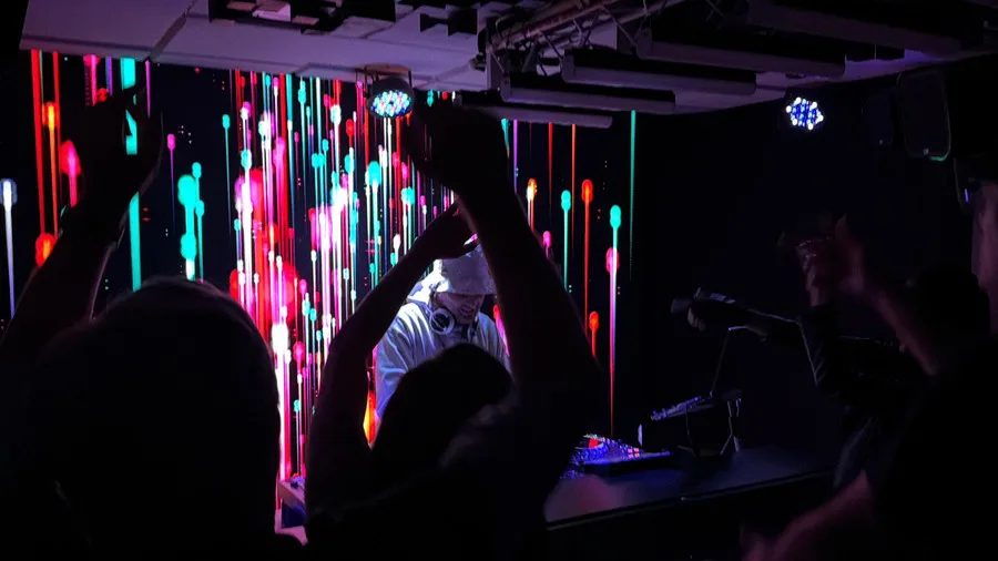 Profissão · DJ tocando para o público de braços erguidos, com painel de LED atrás da cabine